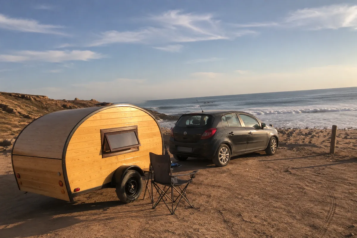 Caravane teardrop garée sur une plage marocaine de la côte atlantique, tractée par une voiture compacte